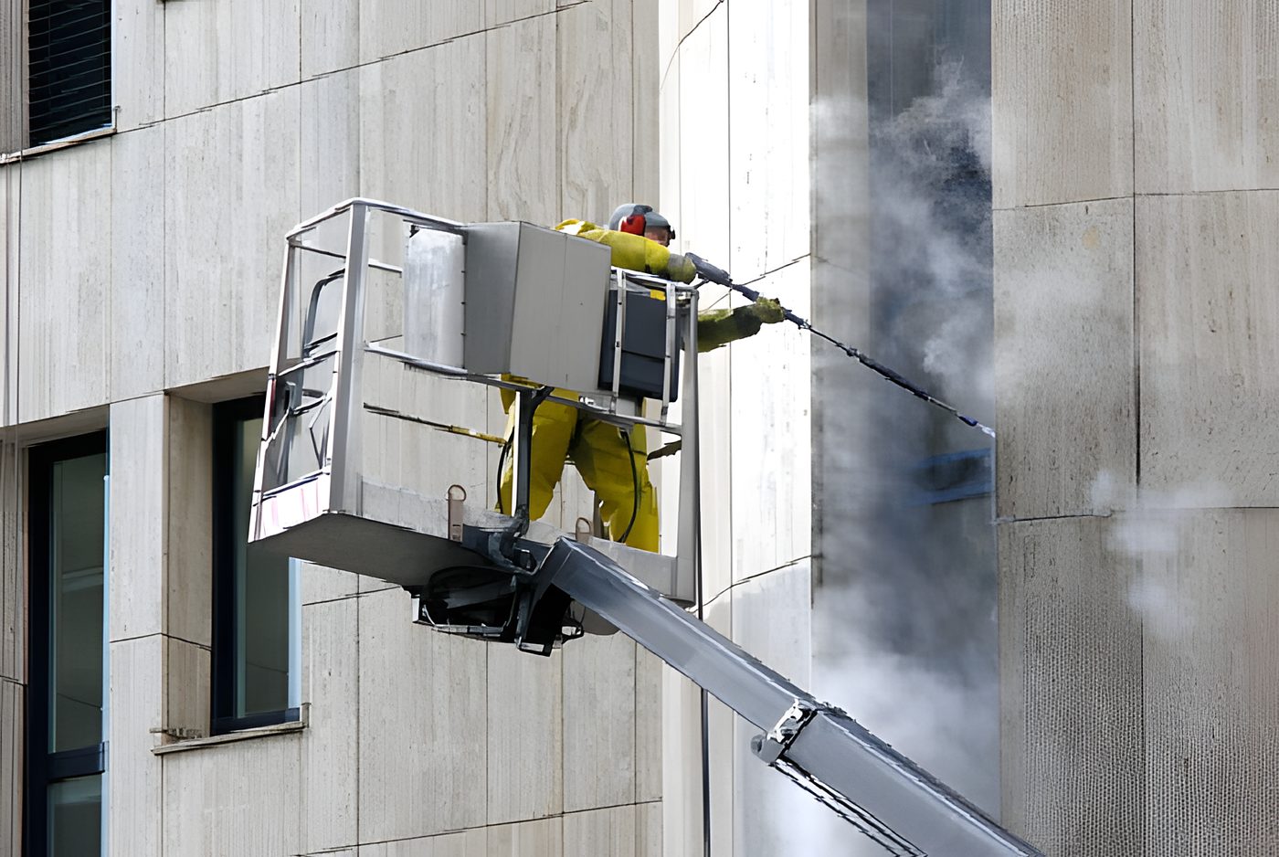 Mitarbeiter im Schutzanzug reinigt eine helle Steinfassade vom Hubsteiger aus