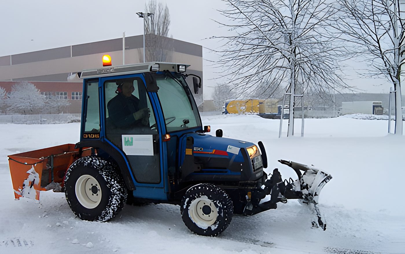 Kleintraktor mit Räumschild im Winterdienst auf einem verschneiten Platz